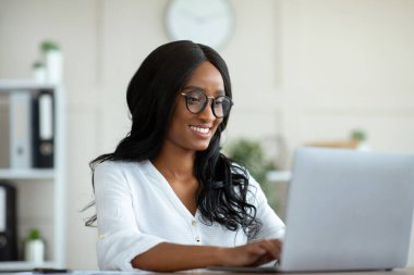 Ofisteki klavyede dizüstü bilgisayar ve daktilo kullanan mutlu kadın şirket çalışanı.