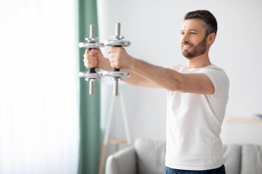 Atletik adam oturma odasının iç tarafına dambılları kaldırıyor.