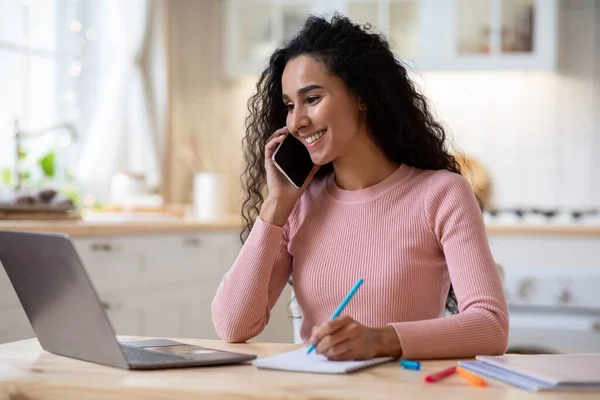 Work From Home. Young Freelancer Lady Using Laptop And Cellphone In Kitchen