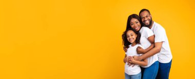 Afro-Amerikalı bir adam karısını kucaklıyor ve gülümsüyor.