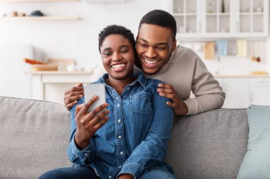 Kanepede oturan siyah çift akıllı telefon kullanıyor.