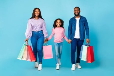 Afro-Amerikan kadın, erkek ve kız alışveriş torbalarıyla yürüyorlar.