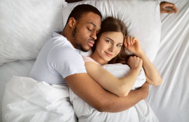 Genç siyah adam uyuyor ve beyaz güzel kız arkadaşına sarılıyor.