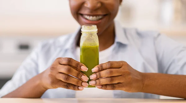 Unrecognizable Black Woman Showing Smoothie Bottle Posing In Modern Kitchen
