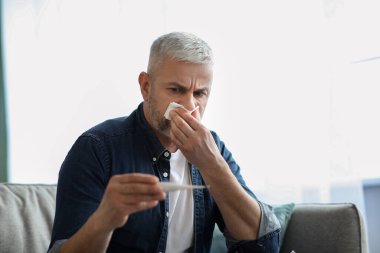 Hasta kıdemli adam hapşırıyor ve ateşi kontrol ediyor.