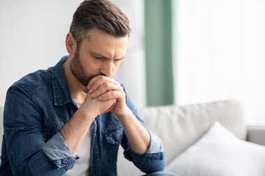 Evdeki kanepede oturan üzgün adamın yakın çekimi.