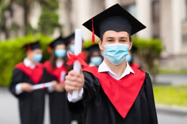 Mezuniyet kostümü giymiş beyaz çocuk diplomasını gösteriyor.