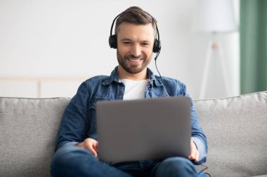 Rahat adam film izliyor, dizüstü bilgisayar ve kulaklık kullanıyor.