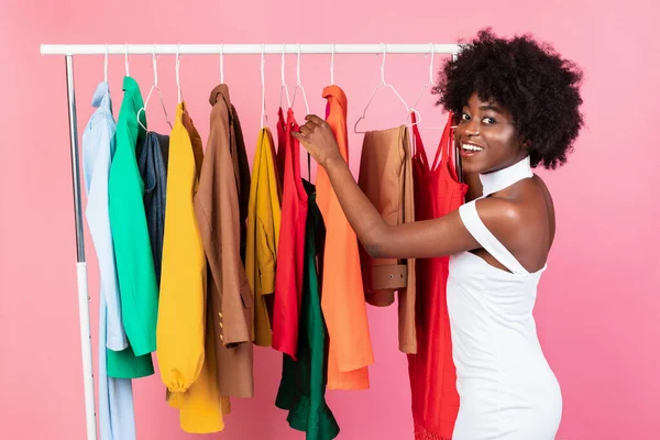 Afrikanische Dame, die Kleidung pflückt, posiert in der Nähe der Kleiderschiene, rosa Hintergrund — Stockfoto