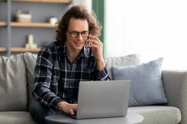 Evde oturan dizüstü bilgisayarla cep telefonuyla konuşan serbest çalışan adam.