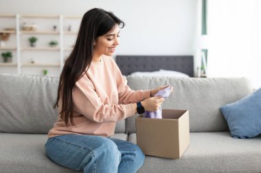 İnternetten alışveriş yaptıktan sonra paketleri açan gülümseyen genç bayan.