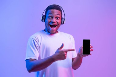 Online Müzik Platformu. Siyah akıllı telefonu işaret eden kulaklıklı heyecanlı Afrikalı adam