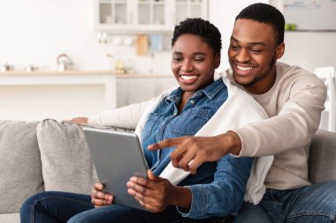 Afro-Amerikan çift kanepede oturuyor, tablet kullanıyorlar.