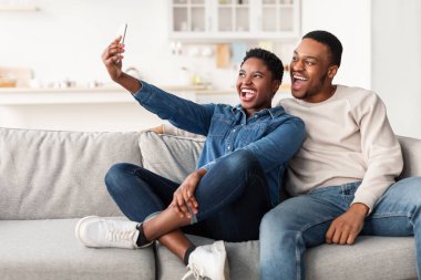 Siyahi bir çiftin evde selfie çekerken portresi.