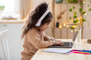 Çevrimiçi Ders. Kulaklık takan ve mutfakta dizüstü bilgisayar kullanan güzel bir kız.