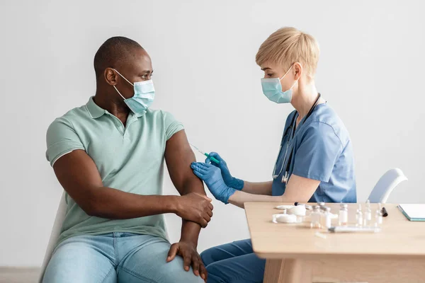 Female nurse in gloves and mask making COVID-19 vaccination in shoulder of adult male — Stock Photo, Image