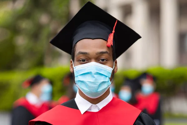 African american guy in graduation costume and face mask, closeup