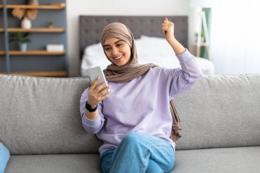 Heyecanlı Müslüman kadın cep telefonu kullanıyor, online galibiyeti kutluyor