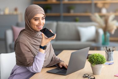 Müslüman kadın cep telefonunda ses asistanı kullanıyor