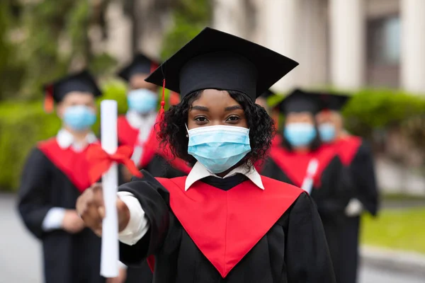 African american young lady in graduation costume and face mask