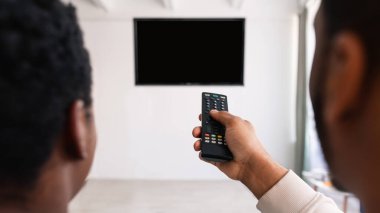 Televizyon izleyen ve uzaktan kumanda kullanan siyah bir çift.