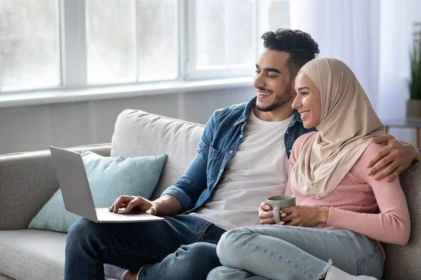 Relaxed arab man and woman watching movie on laptop