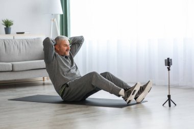 Yetişkin adam evde eğitim görüyor, akıllı telefonu tripodda kullanıyor.