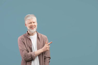 Güzel teklif. Kendine güvenen albino adam turkuaz stüdyo arka planında boş alana bakıyor ve kameraya gülümsüyor.