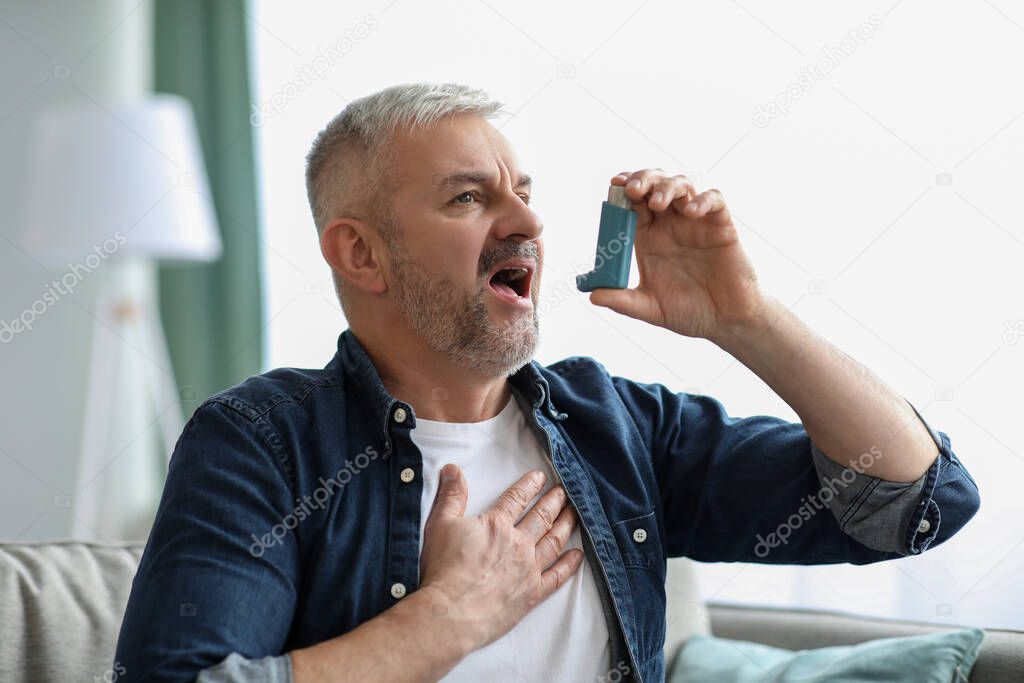Senior man touching chest and using inhaler