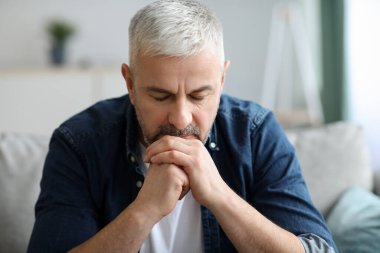 Düşünceli kıdemli adam koltukta oturuyor, aşağı bakıyor.