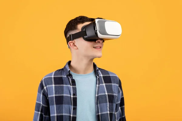 Cool guy in VR headset exploring cyberspace, using virtual reality for entertainment or studies on orange background — Stock Photo, Image