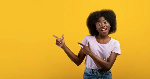 Sehen Sie hier. Junge Afroamerikanerin zeigt auf Kopierraum über gelbem Studiohintergrund — Stockfoto