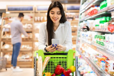 Süpermarkette akıllı telefon kullanan Orta Doğulu Mutlu Kadın Market alışverişi yapıyor