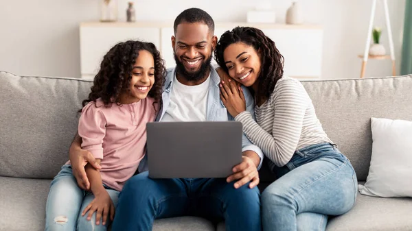 Felice famiglia afroamericana utilizzando il computer portatile seduto sul divano — Foto Stock