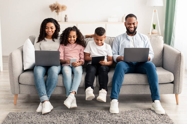 Happy african american family holding and using personal gadgets