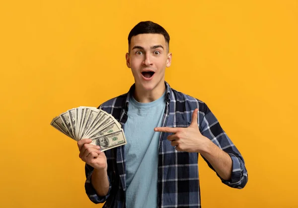 Emocional joven en ropa casual apuntando a los fanáticos de los billetes de dinero en fondo de estudio naranja —  Fotos de Stock