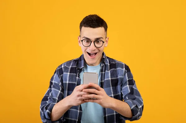 Pemuda funky menggunakan ponsel untuk komunikasi online, bekerja atau belajar di latar belakang studio oranye — Stok Foto