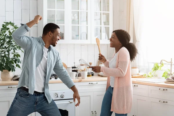 Diversión doméstica. Cónyuges negros peleando juguetonamente en la cocina, usando espátulas como armas — Foto de Stock