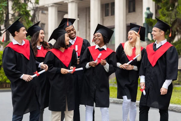 Graduados felices en trajes de graduación riendo, celebrando el éxito —  Fotos de Stock