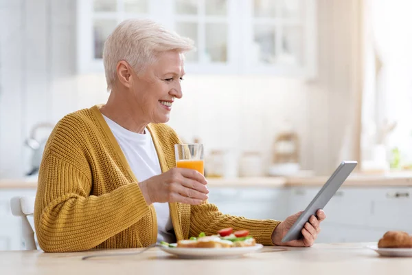 Fröhliche Seniorin mit digitalem Tablet beim Mittagessen, Seitenansicht — Stockfoto