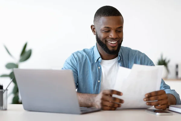 Χαρούμενος νεαρός μαύρος επιχειρηματίας που εργάζεται με έγγραφα στο σύγχρονο γραφείο — Φωτογραφία Αρχείου
