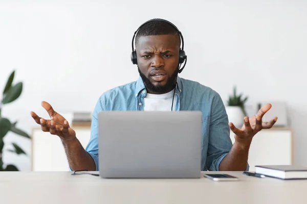 Praca w stresie. irytujący czarny człowiek w zestaw słuchawkowy patrząc na laptop ekran — Zdjęcie stockowe