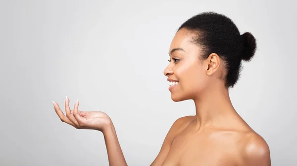 Zwarte vrouw met onzichtbare cosmetica pot reclame product, grijze achtergrond — Stockfoto