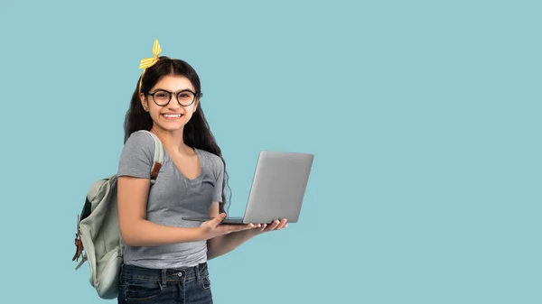 Retrato de menina adolescente indiana usando computador portátil, estudando on-line no fundo do estúdio azul, banner com espaço de cópia — Fotografia de Stock