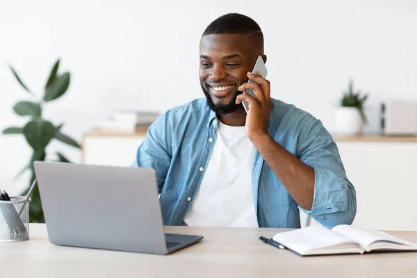 Afstandsbediening. Zwarte Freelancer Guy met behulp van mobiele telefoon en laptop op het thuiskantoor — Stockfoto