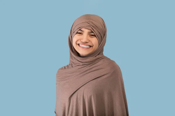 Portrait of positive Muslim teen girl in hijab smiled at camera over blue studio background — Stok Foto