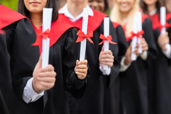 Diplomás végzősök felismerhetetlen multiracionális csoportja, akik oklevéltekercset, közelképet mutatnak — Stock Fotó