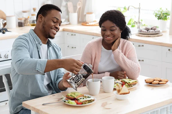 Afectuosa pareja negra comiendo sabroso desayuno y beber café en la cocina — Foto de Stock