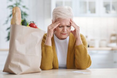 Mutfakta market faturasını kontrol eden yaşlı bir kadın.