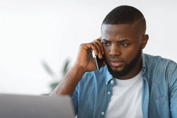 Portrait de l'homme africain occupé parlant sur téléphone portable et travaillant sur ordinateur portable — Photo